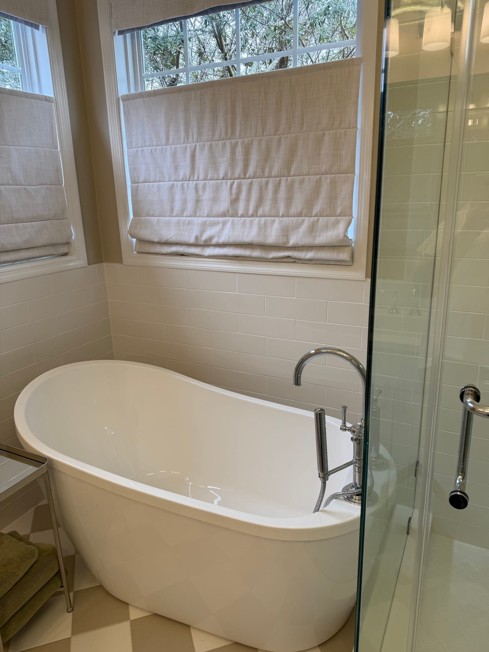 Freestanding tub beneath a roman blind, glass shower enclosure alongside and checkerboard tile underfoot