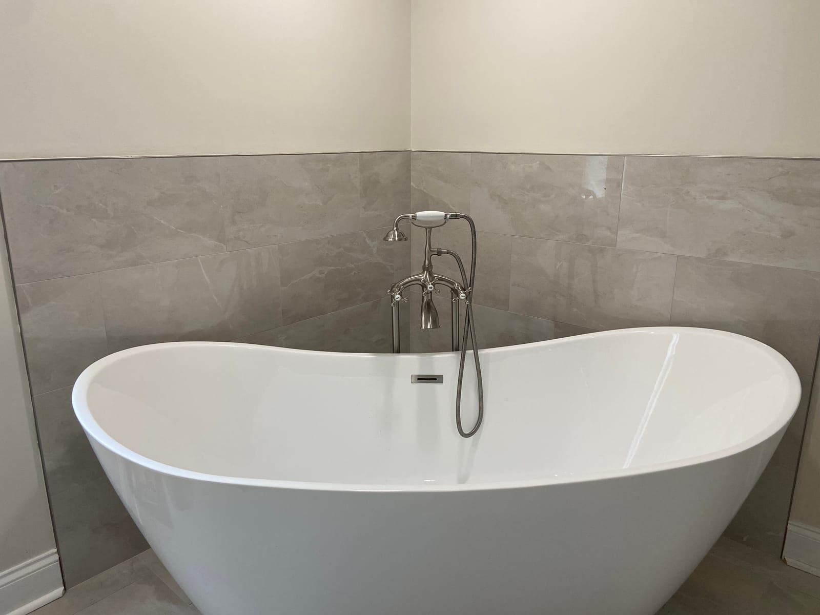 Freestanding tub against grey large-format wall tile in a completed bathroom remodel