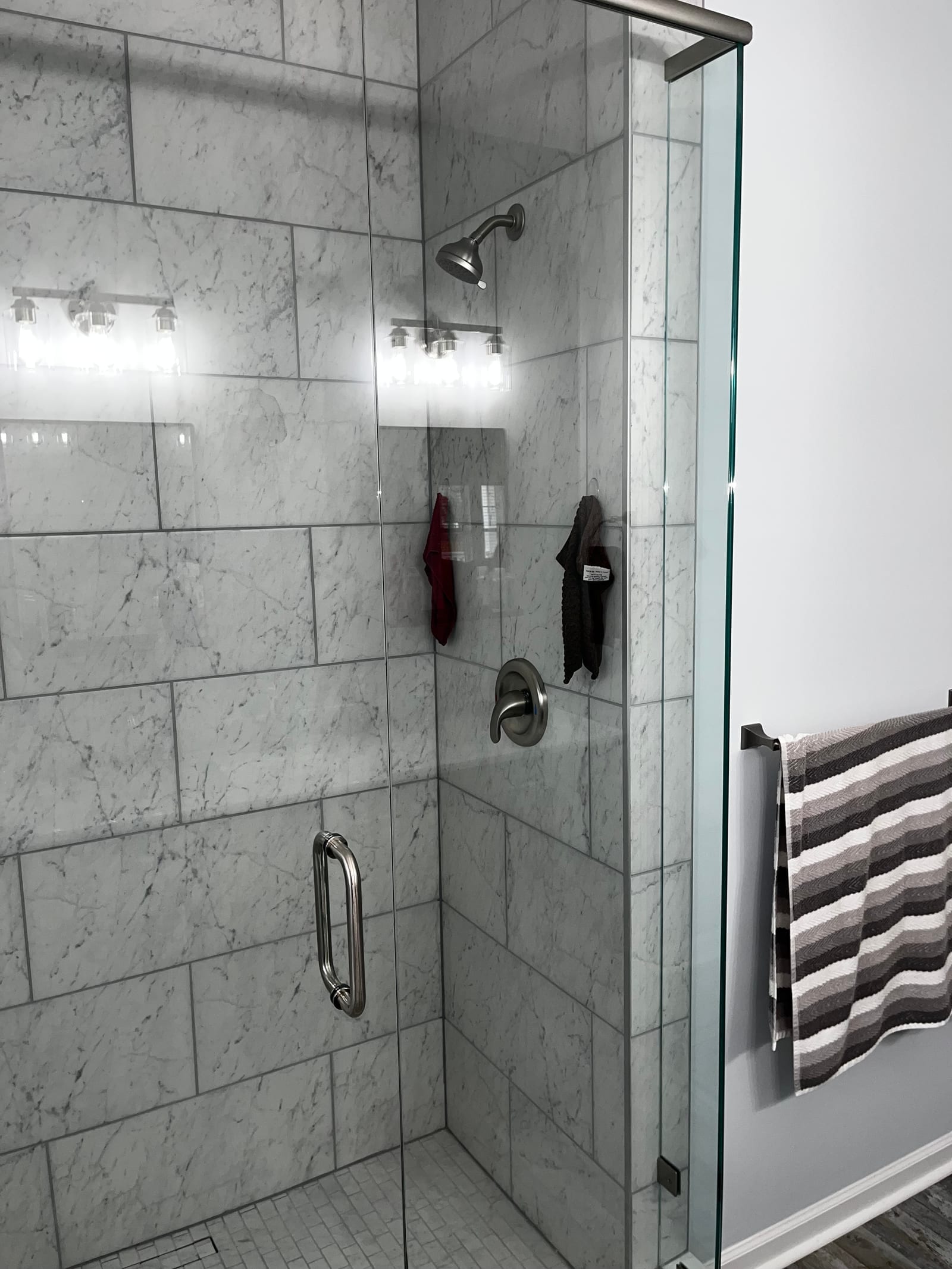 Walk-in shower finished in large-format marble-look tile with a glass enclosure and a heated towel rail alongside