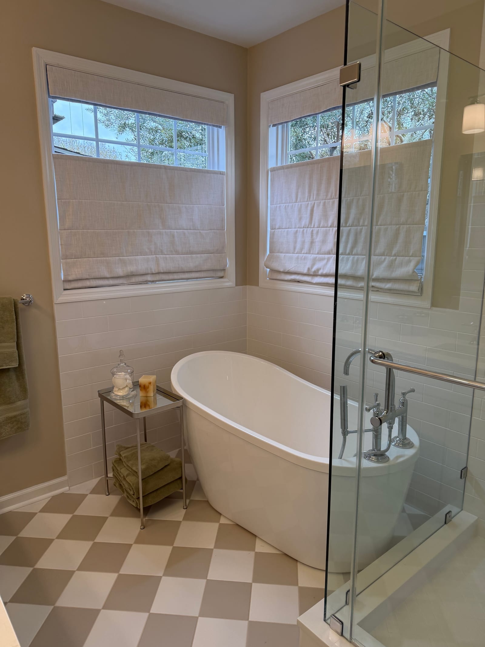 Freestanding slipper tub set between two windows in a finished bathroom remodel, with a polished nickel floor-mounted filler