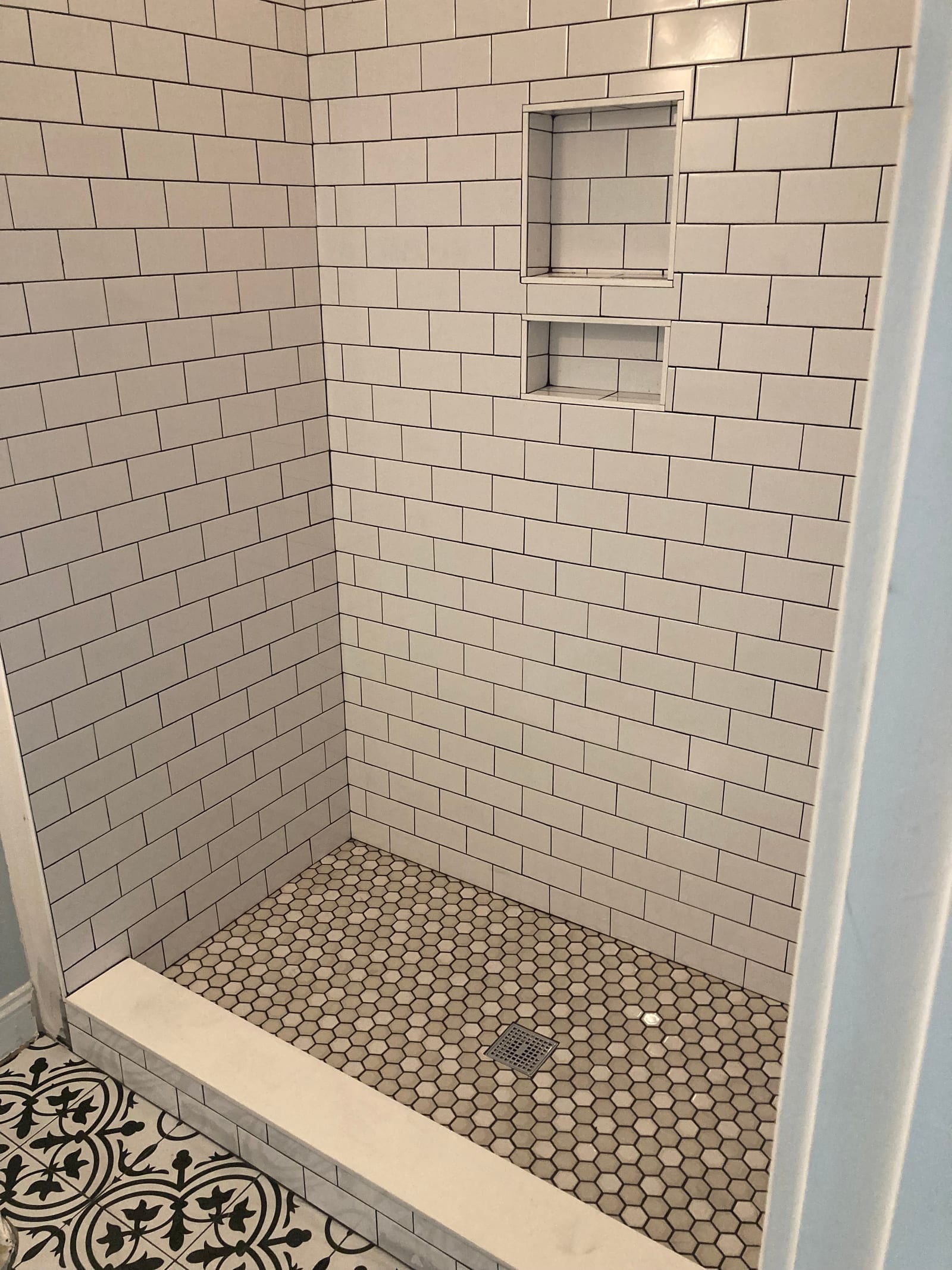 White subway tile shower with two recessed shampoo niches and a hexagonal mosaic tile floor
