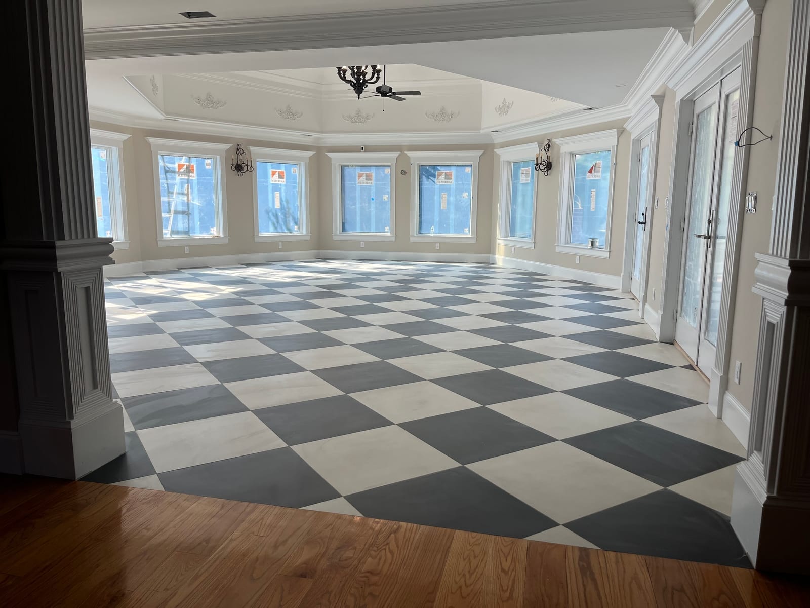 Checkerboard tile floor laid in a bay-windowed room, meeting refinished hardwood at the threshold