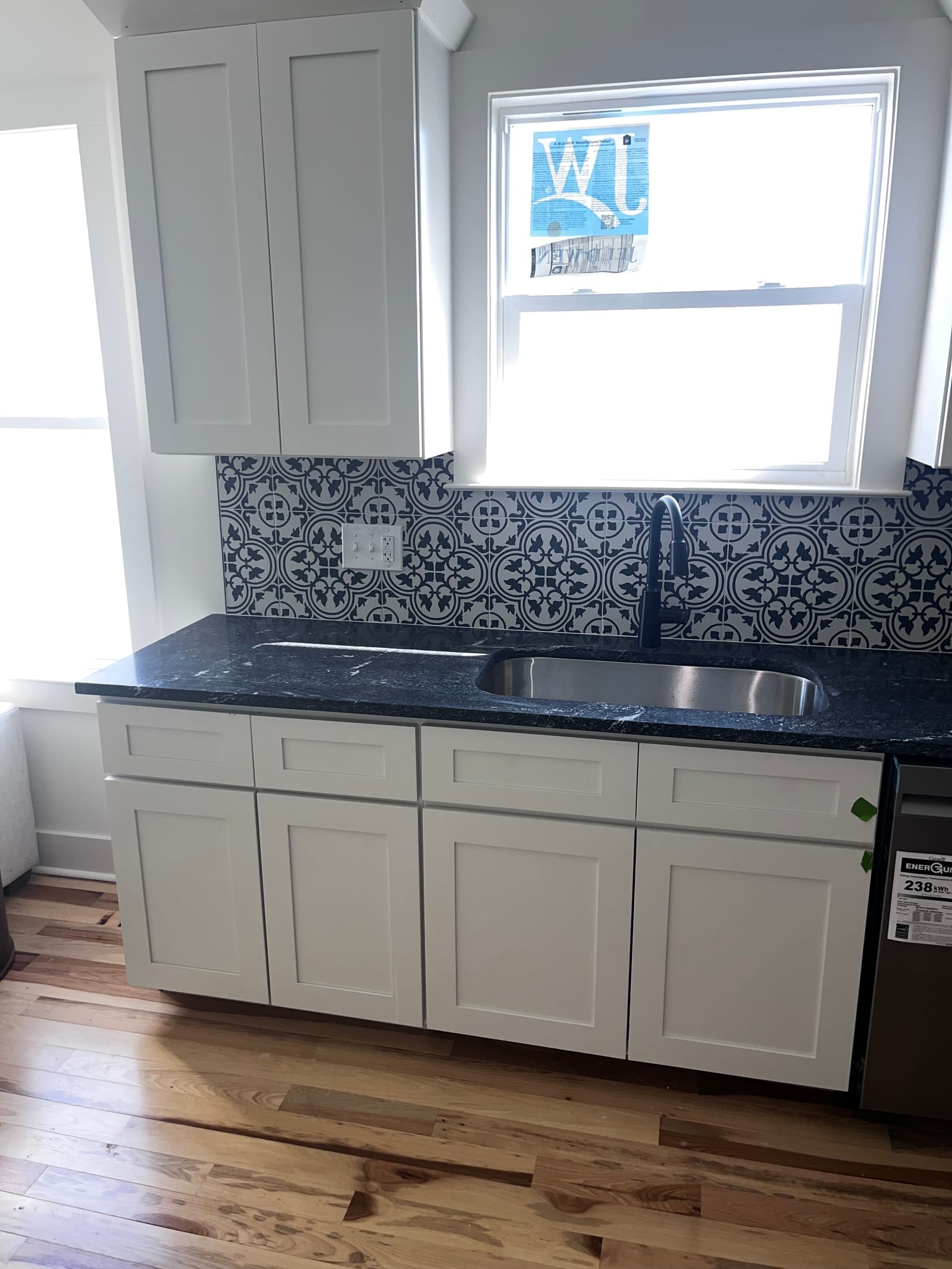 Kitchen with white shaker cabinets, a dark granite worktop and a patterned blue and white tile backsplash
